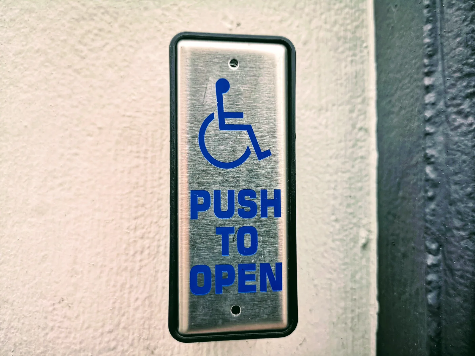 Close-up of a push button sign for accessibility on a white wall. The short version of accessible attraction planning cost