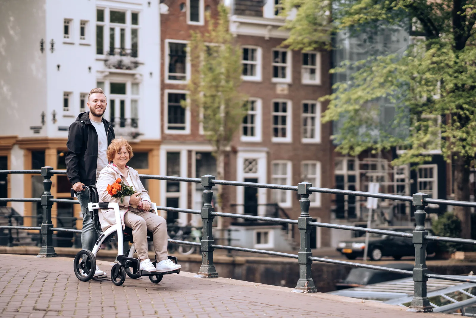 A senior woman in a wheelchair with flowers enjoys a stroll along Amsterdam's iconic canals. Accessible travel budgets booking: questions to ask
