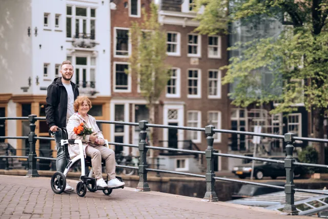A senior woman in a wheelchair with flowers enjoys a stroll along Amsterdam's iconic canals. Accessible travel budgets booking: questions to ask