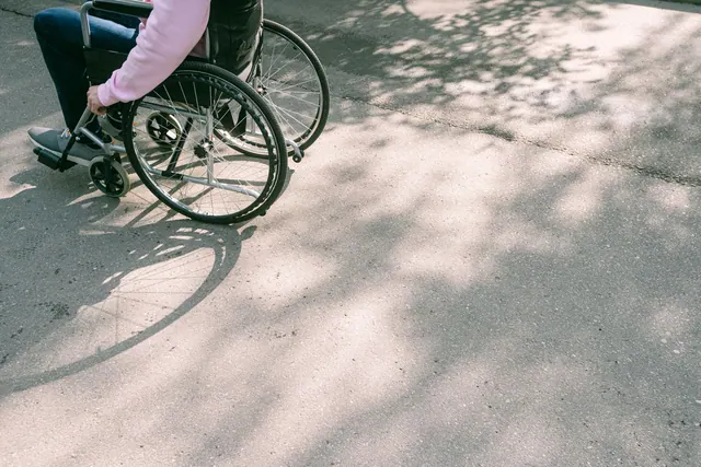 A person in a wheelchair navigating a sunlit road with tree shadows. The image captures a moment of mobility and independence.
