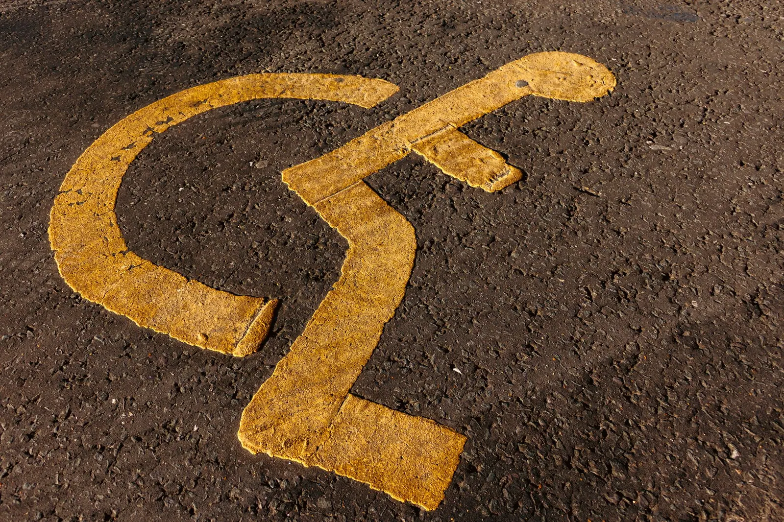 Close-up of a yellow wheelchair accessibility symbol on textured asphalt.