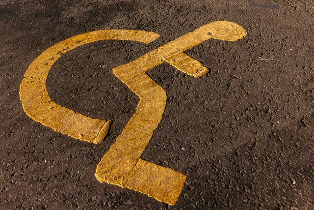 Close-up of a yellow wheelchair accessibility symbol on textured asphalt.