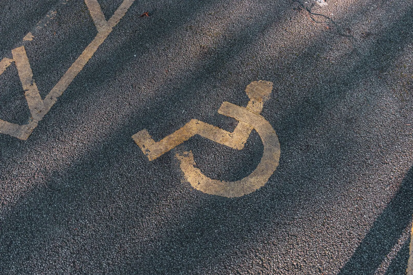 Close-up of an asphalt parking spot with a yellow wheelchair symbol for accessibility.