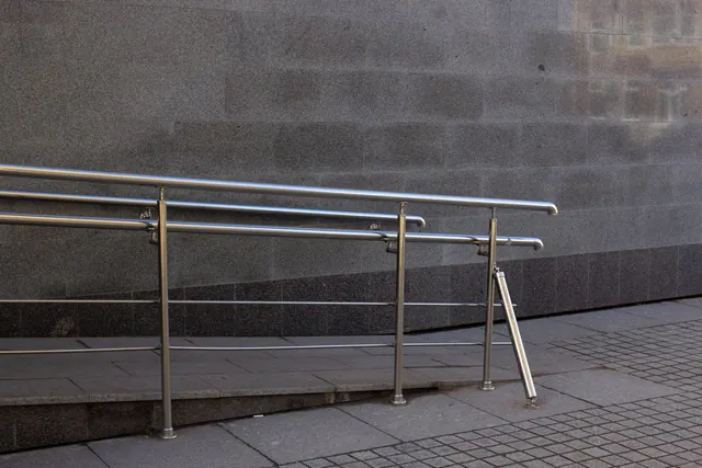 Close-up of a metal handrail and concrete ramp for accessibility in an urban setting.
